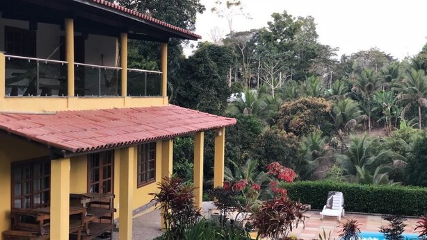 Un bâtiment jaune avec un toit rouge, une piscine et une végétation luxuriante.