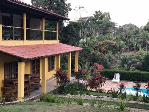 A yellow building with a red roof, a pool, and lush greenery.