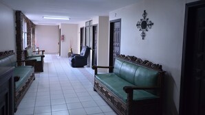 A hallway with a green sofa, a black chair, and a wooden cabinet. - Hotel Suites del Sol (Tijuana)