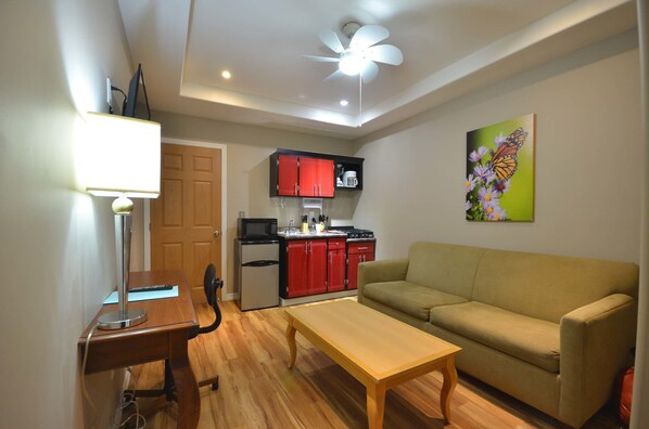 A compact living space with a kitchenette, a dining table, a sofa, and a ceiling fan.