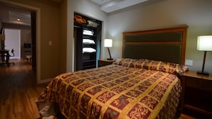 A bedroom with a large bed, a wooden headboard, a nightstand with a lamp, and a closet with folded clothes. - Hotel Suites del Sol (Tijuana)