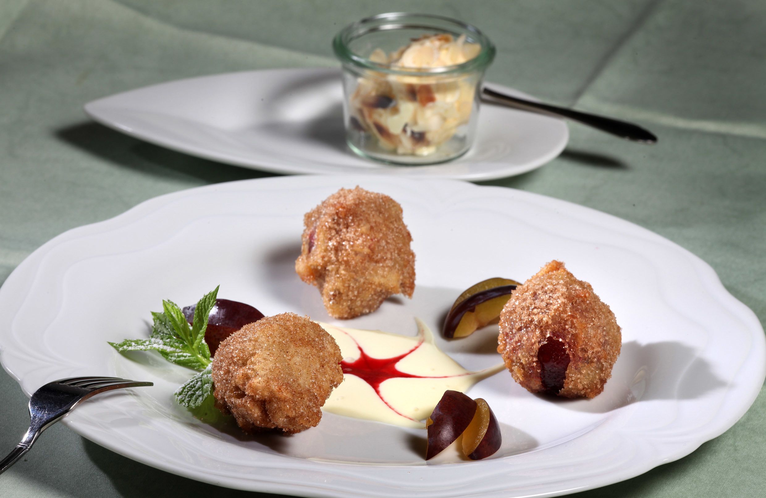 Un plato con tres preparaciones rebozadas y un vaso pequeño de postre sobre una fuente blanca.