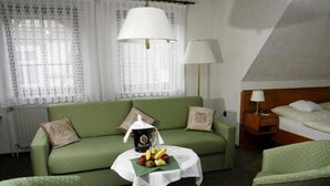 A hotel room with a green sofa, a small table with fruits, a lamp, and a bed. - Hotel Restaurant Pempel (Grossalmerode)