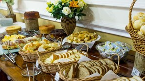 A buffet table with various breads, pastries, and a flower arrangement.