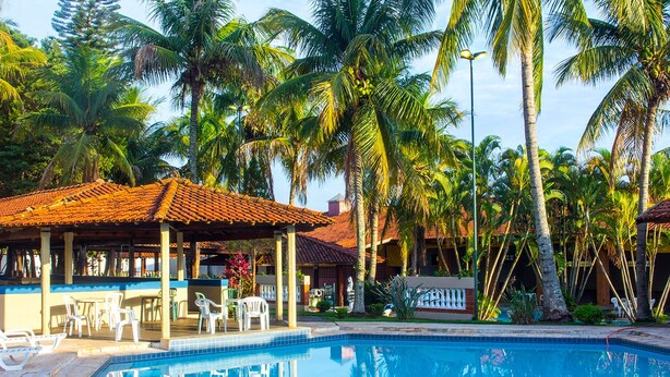 A pool area with a tiled deck, lounge chairs, and a covered seating area with a tiled roof.