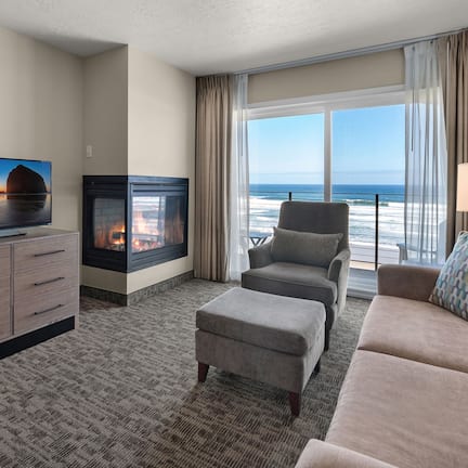 A hotel room with a fireplace, a sofa, a TV, and a view of the ocean.