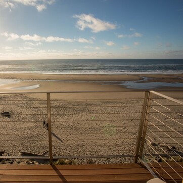 A beach view from a wooden deck with a metal railing.
