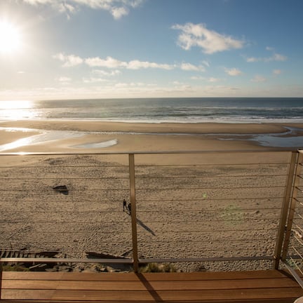 A beach view from a wooden deck with a metal railing.