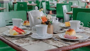 Een eetgedeelte met groene stoelen en tafels, wit servies en diverse soorten eten.