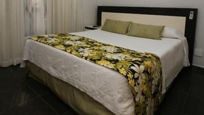 Hotelkamer met een bed, een raam met gordijnen, een airconditioning en een foto in een lijst aan de muur.