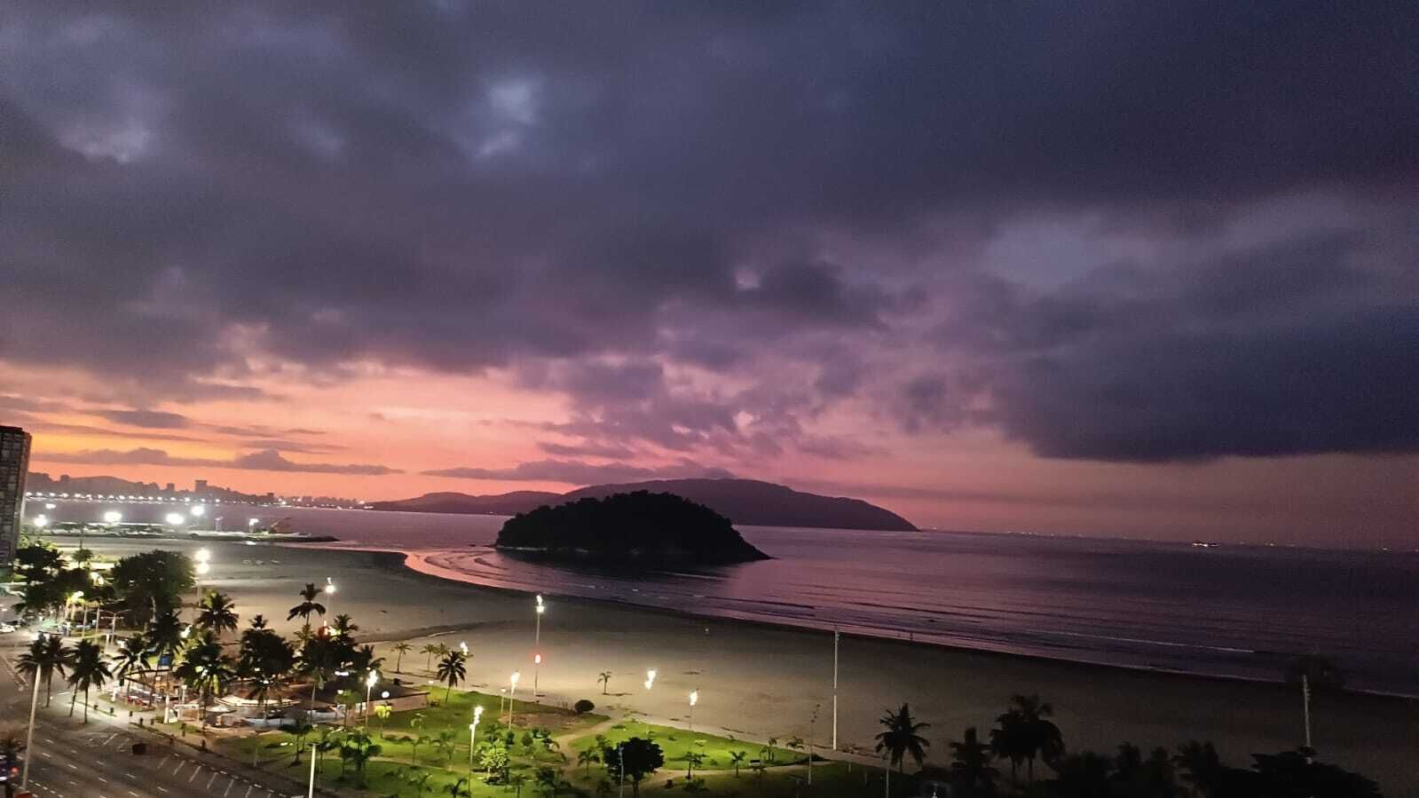 A coastal view with a beach, palm trees, and a distant island under a twilight sky.