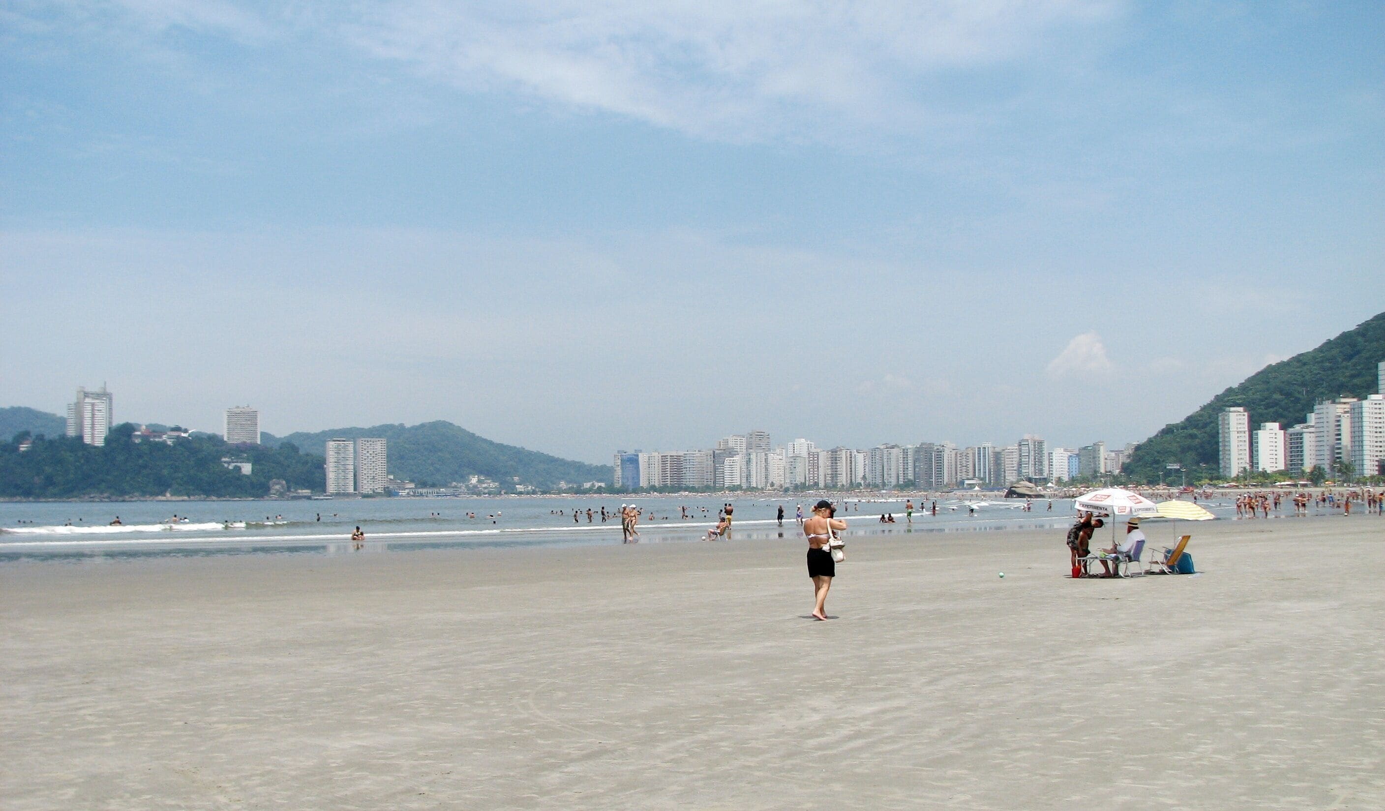 Una playa con gente, sombrillas y edificios al fondo.