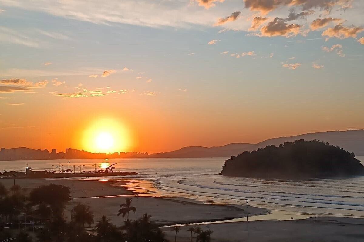 Un coucher de soleil sur une plage, avec une île lointaine à l’horizon, des eaux calmes et un ciel dégagé.