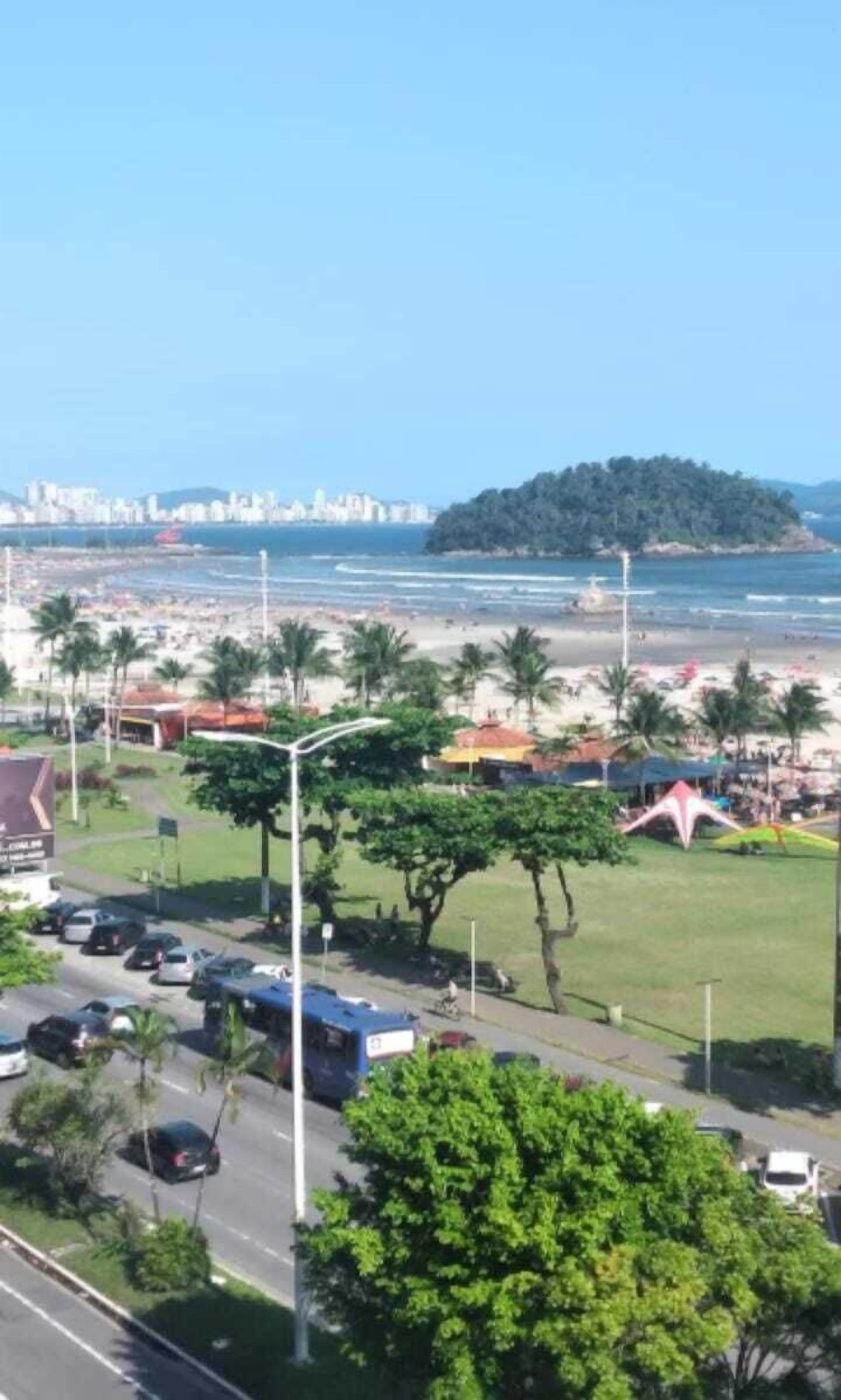 A coastal view with a beach, a road with parked cars, and a distant cityscape.