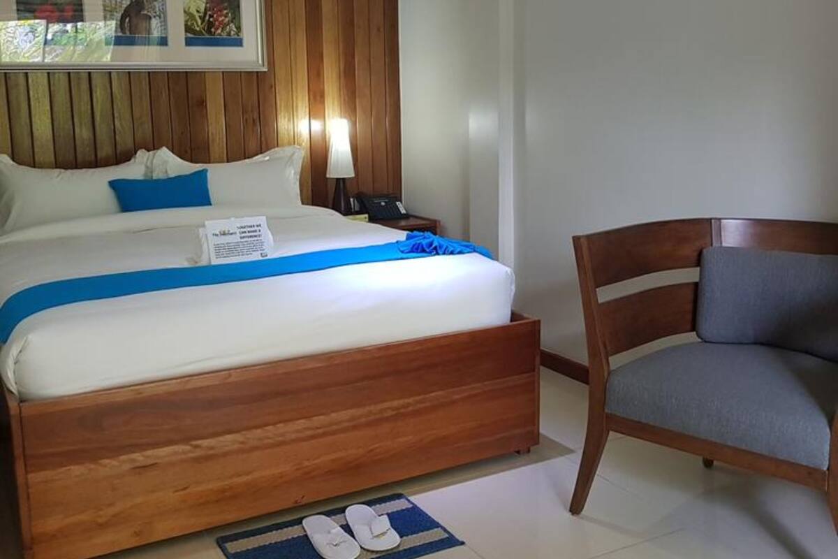 Ein Hotelzimmer mit einem hölzernen Bett, einem Nachttisch, einem Sessel und einem gerahmten Bild an der Wand.