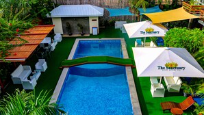 Zona de piscina con una pequeña piscina, sillas de descanso, sombrillas y un edificio con la inscripción 'The Sanctuary Hotel Resort Spa'.