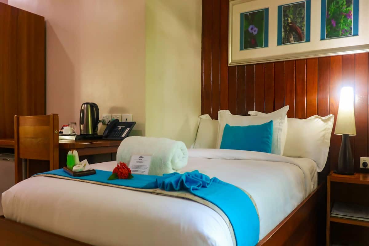 Ein Hotelzimmer mit einem ordentlich bezogenen Bett, einem Schreibtisch mit Telefon und Kaffeemaschine sowie einer Wand mit gerahmten Bildern.