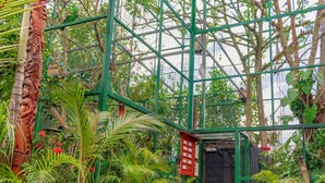 Un invernadero con estructura metálica, plantas en macetas y un panel informativo rojo.