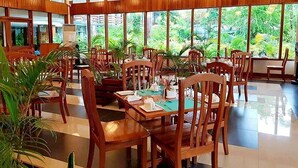 Un restaurante con mesas y sillas de madera, amplios ventanales que dan a zonas verdes, y lámparas esféricas colgantes.