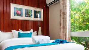 Una cama bien hecha con ropa de cama blanca y azul, un cuadro enmarcado encima y una ventana con cortinas.