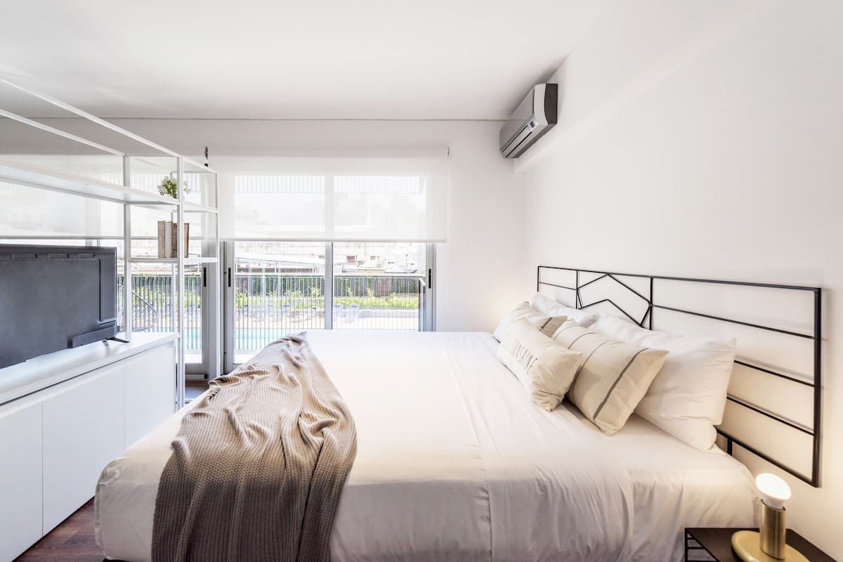 A modern hotel room with a large bed, a TV, and a balcony with a view of the city.