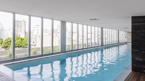 An indoor swimming pool with a wooden deck and large windows offering a city view. - Top Rentals Dorrego (Buenos Aires)