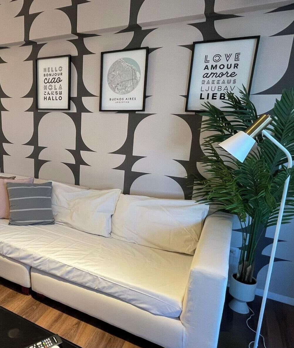 Un canapé blanc agrémenté de plusieurs coussins, un lampadaire et une plante en pot, le tout dans une pièce dont le mur est décoré d’un motif.