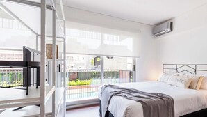 A modern bedroom with a large bed, a view of the city, and an air conditioning unit. - Top Rentals Dorrego (Buenos Aires)