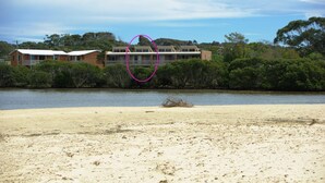 Une propriété située en bord de mer, avec une plage de sable, une étendue d’eau et un bâtiment doté d’un balcon.