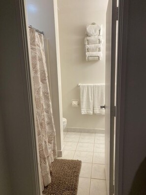 A bathroom with a shower curtain, a towel rack with towels, and a toilet.
