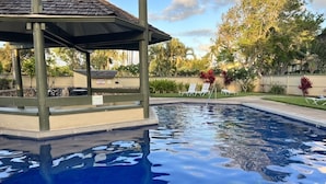 Piscina com gazebo, espreguiçadeiras e paisagismo tropical.