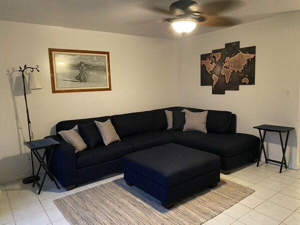 A living room with a black sectional sofa, a matching ottoman, a floor lamp, and a world map artwork on the wall.