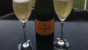A bottle of Veuve Clicquot champagne and two glasses on a table with a view of a pool and palm trees. - Ocean Front Luxury 2/2 in Whispering Seas (Tower isles)