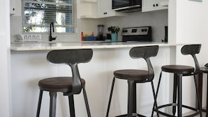 A kitchen with white cabinets, a black microwave, and three bar stools with dark seats. - Ocean Front Luxury 2/2 in Whispering Seas (Tower isles)