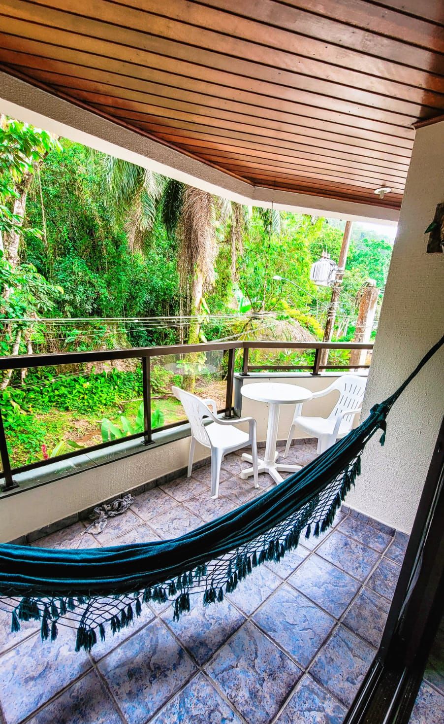 Un balcon avec un hamac, des chaises blanches et une vue sur une végétation luxuriante.