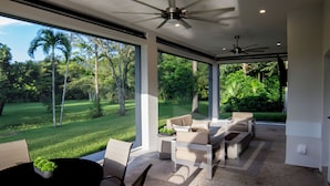 A modern outdoor living area with a ceiling fan, large windows, and a view of a lush garden. - COUNTRY ESTATE IN QUIET UPSCALE COMMUNITY (Lake Worth)