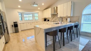 A modern kitchen with a marble countertop, stainless steel appliances, and a large island with bar stools. - COUNTRY ESTATE IN QUIET UPSCALE COMMUNITY (Lake Worth)