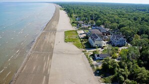 Luftaufnahme einer Küstenlandschaft mit Sandstrand, einer Reihe von Häusern und dichter Vegetation.