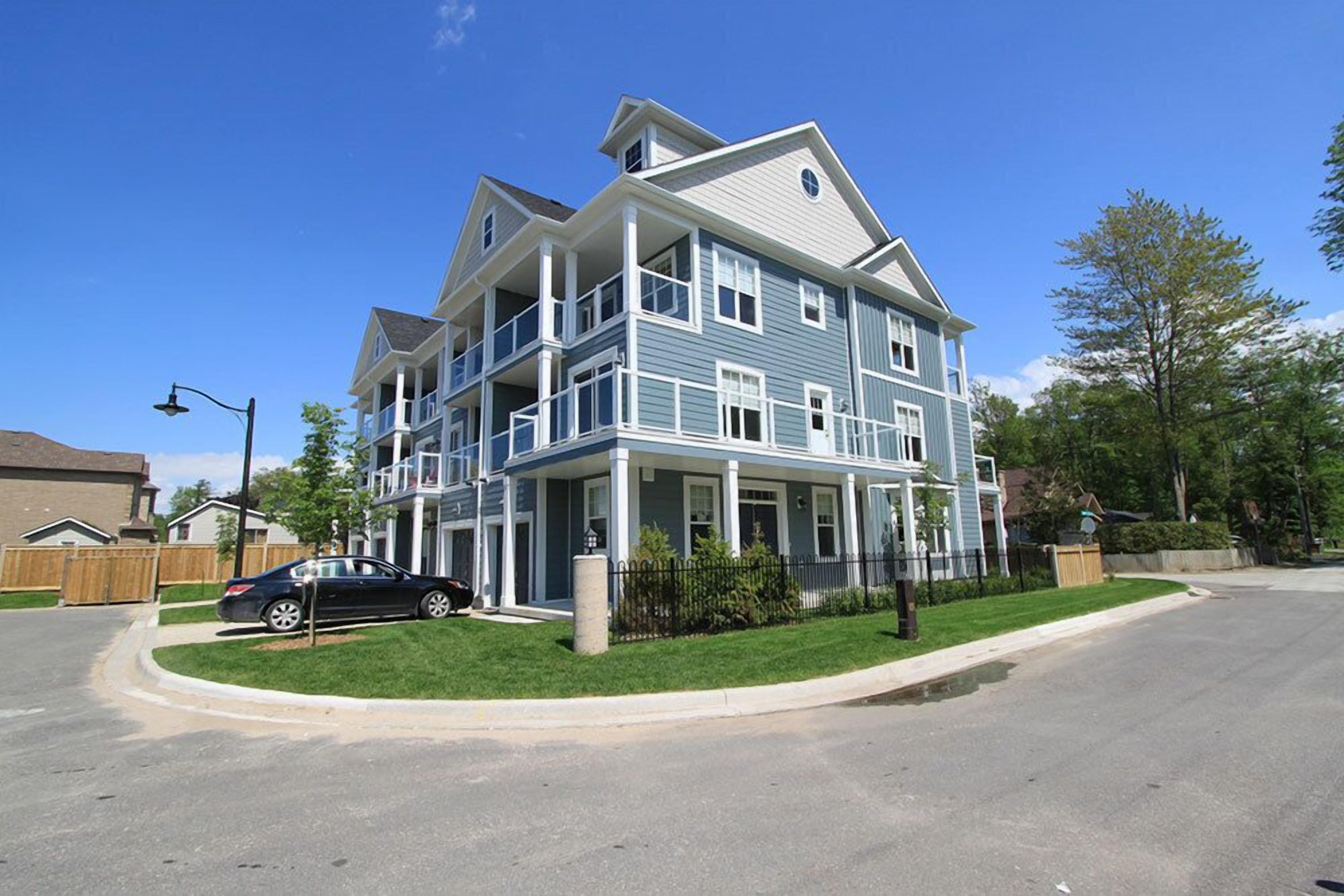A multi-story residential building with a two-story balcony on the second floor, a well-maintained lawn, and a parked car in the driveway.