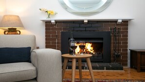 Una sala de estar acogedora con chimenea, un sofá, una mesita con vasos y una lámpara.