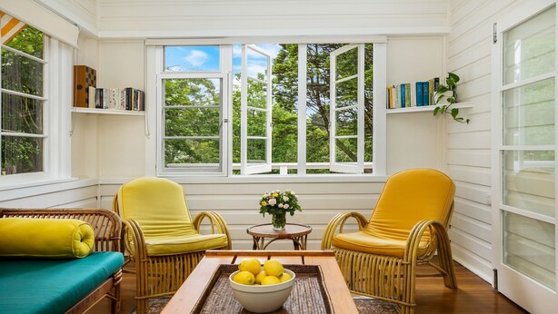 Una habitación luminosa con paredes blancas, dos sillas amarillas, un sofá de mimbre y una mesa con un cuenco de limones.