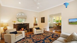 Una sala de estar con chimenea, dos sillones, una mesa de centro, un tapete y un televisor.