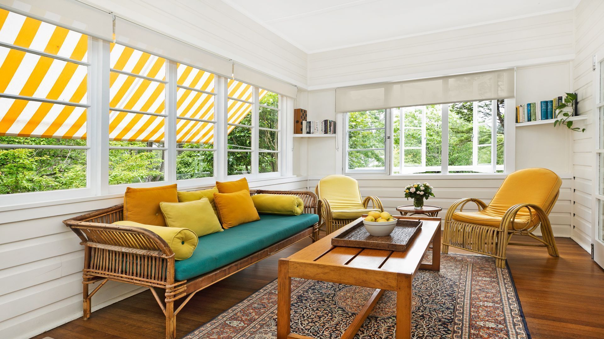 A bright, sunlit room with a wicker sofa, yellow armchairs, and a wooden coffee table.