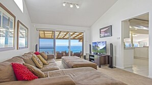 Uma sala de estar com sofá, televisão e vista para o mar.