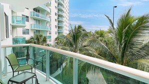 A modern apartment building with balconies, glass railings, and palm trees.
