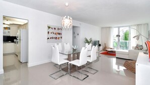 A modern kitchen with white cabinets, a white refrigerator, and a glass dining table with white chairs.