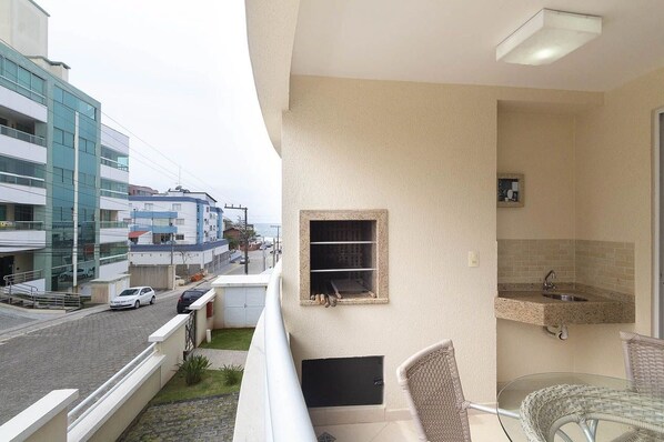 A balcony with a view of the street, a small sink, and a window with a shelf.