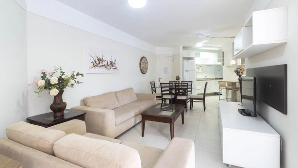 A modern living room with a sofa, coffee table, and a flat-screen TV mounted on the wall. - Vila Maior 207 - Praia de Bombas (Bombinhas)