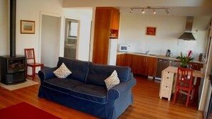 Ein Wohnzimmer mit blauem Sofa, Holzboden, einem roten Teppich, einem Kamin, einer Küche im Hintergrund und einem Essbereich.