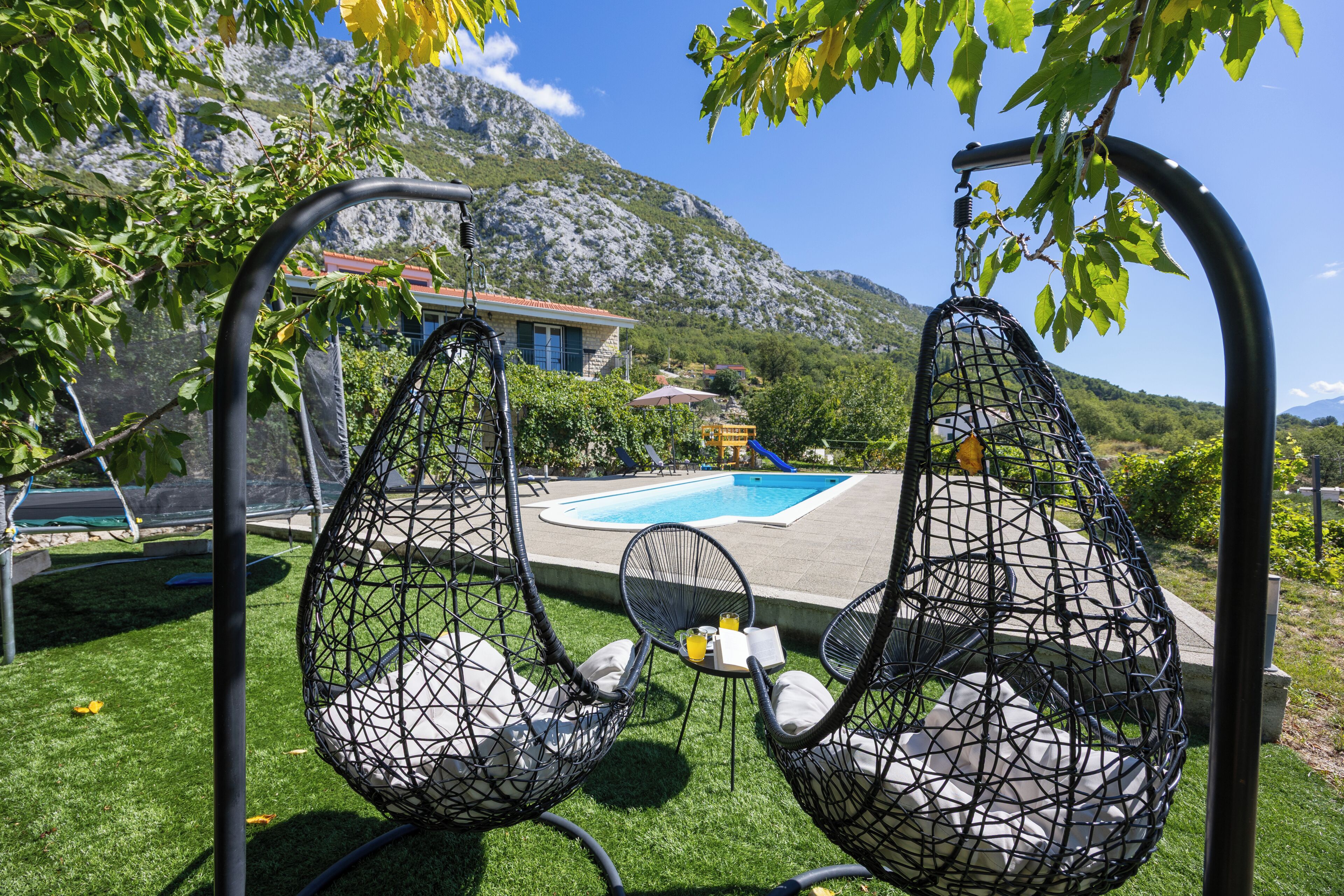 A poolside area with hanging chairs and a view of mountains.
